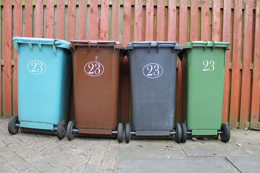 Four colored recycling bins lined up against a wooden fence