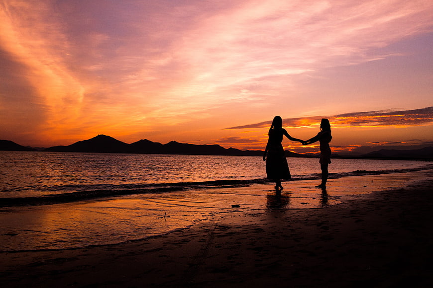 Silhouette of two women holding hands on beach at sunset