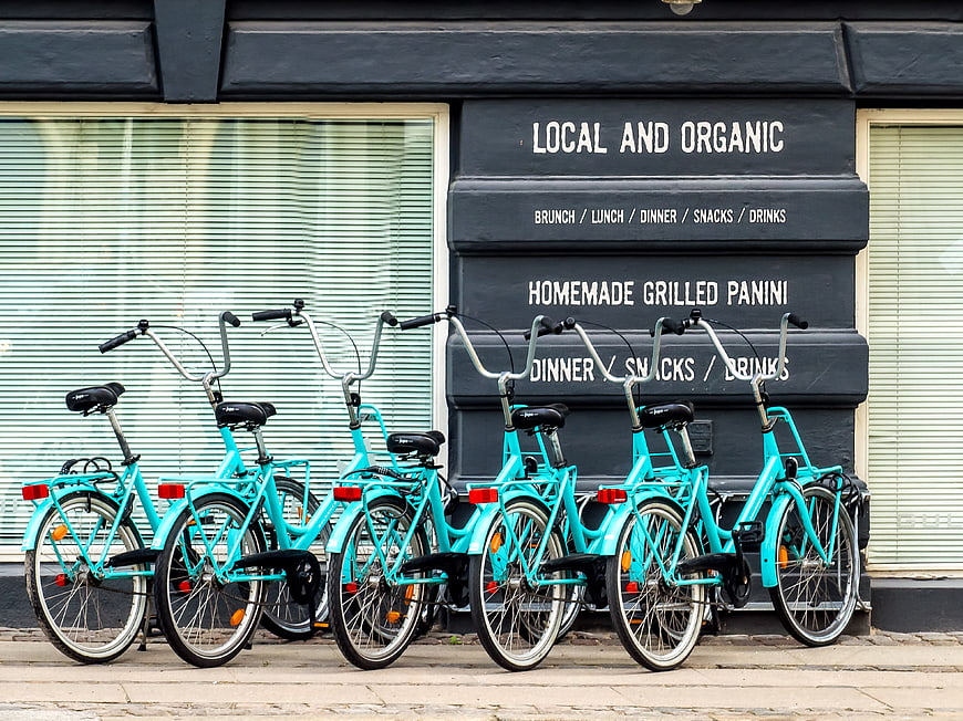 Row of turquoise rental bicycles parked in front of a local organic restaurant facade