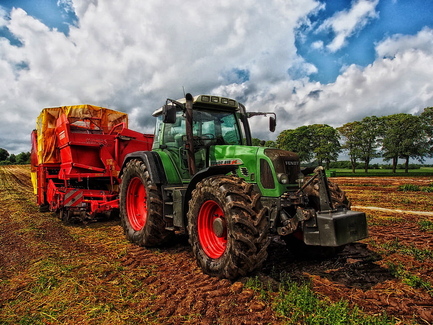 Green Fendt Tractor Pulling Red Harvester in Field