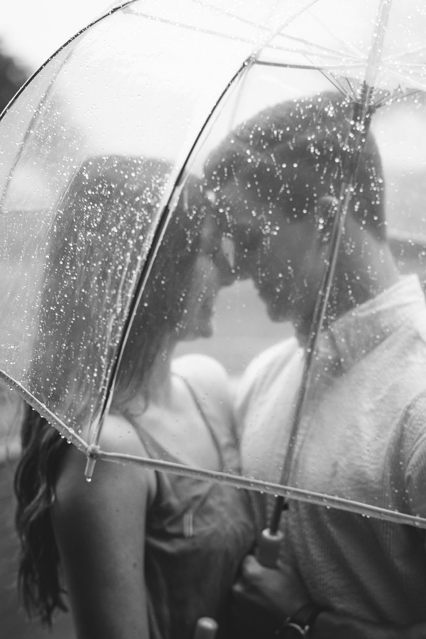Romantic couple kissing under clear umbrella in rain