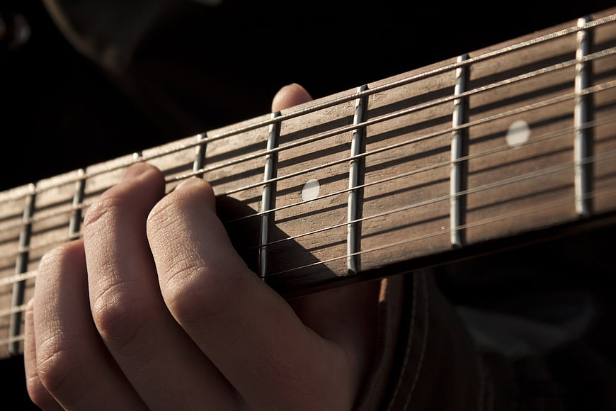 Close-up of hand playing acoustic guitar fretboard