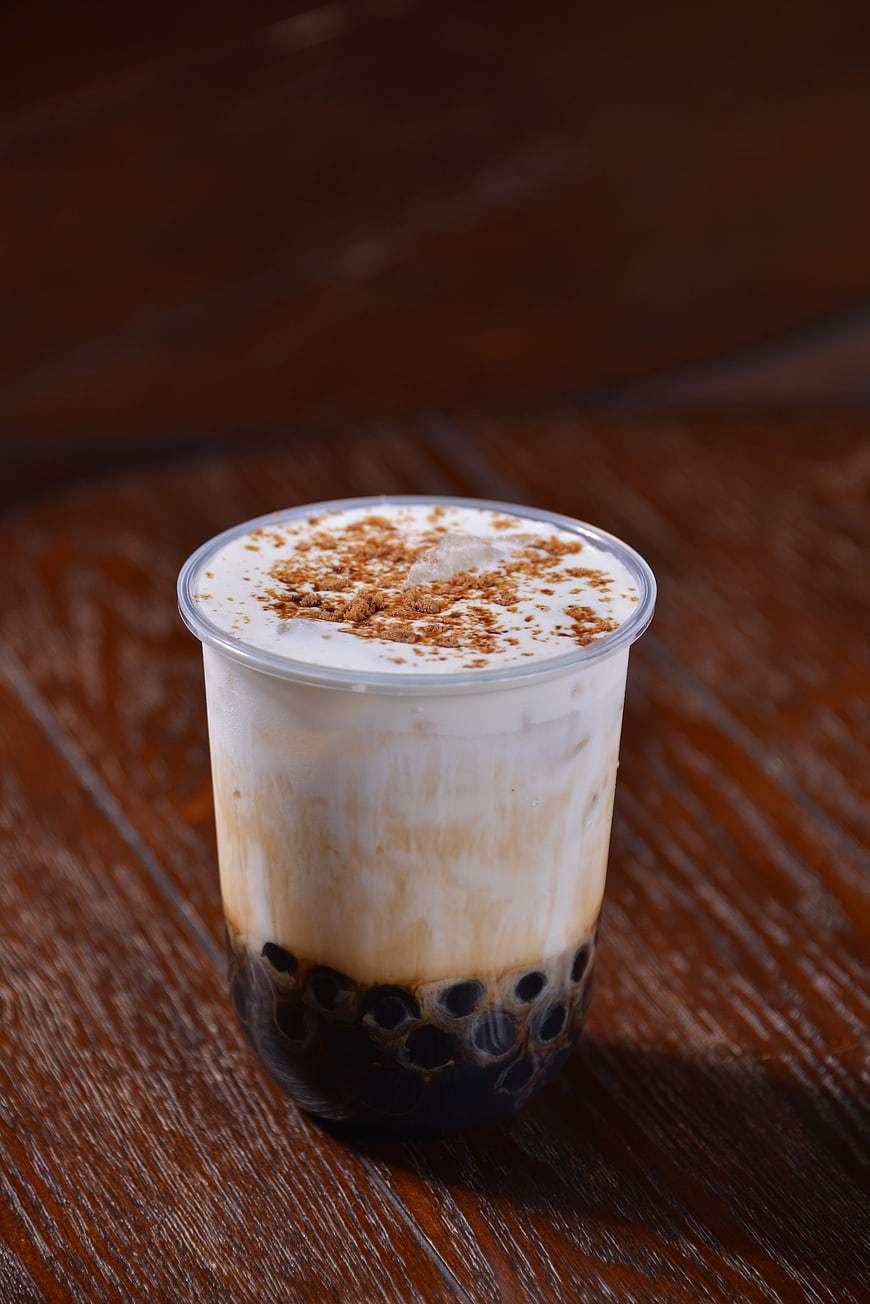 Iced Brown Sugar Pearl Milk Tea in Clear Plastic Cup on Wooden Table