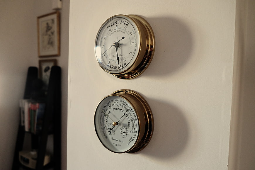 Vintage brass marine tide and barometer gauges on wall