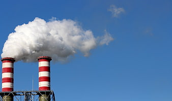 Red and White Industrial Smokestacks Emitting Steam Against Blue Sky