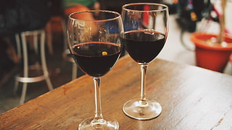 Two glasses of red wine on a rustic wooden table at an outdoor cafe