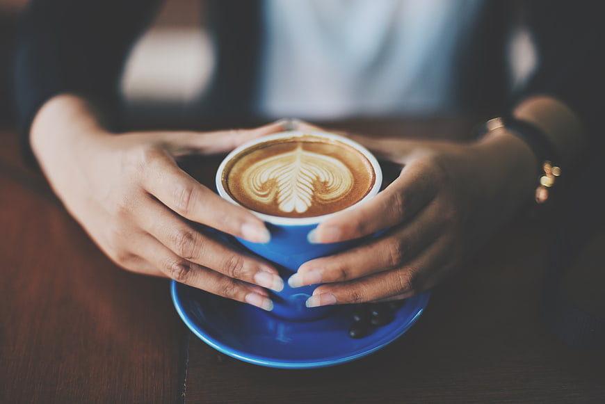 Hands holding blue coffee cup with latte art
