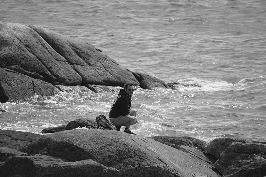 Man Crouching on Rocky Coastline in Black and White