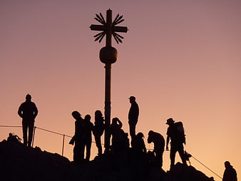 Hikers Silhouetted Against Sunrise at Mountain Summit Cross