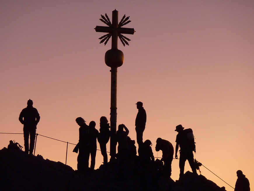 Hikers Silhouetted Against Sunrise at Mountain Summit Cross