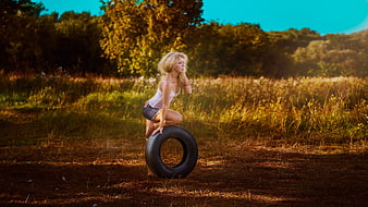 Blonde Woman Kneeling on Tire in Golden Field