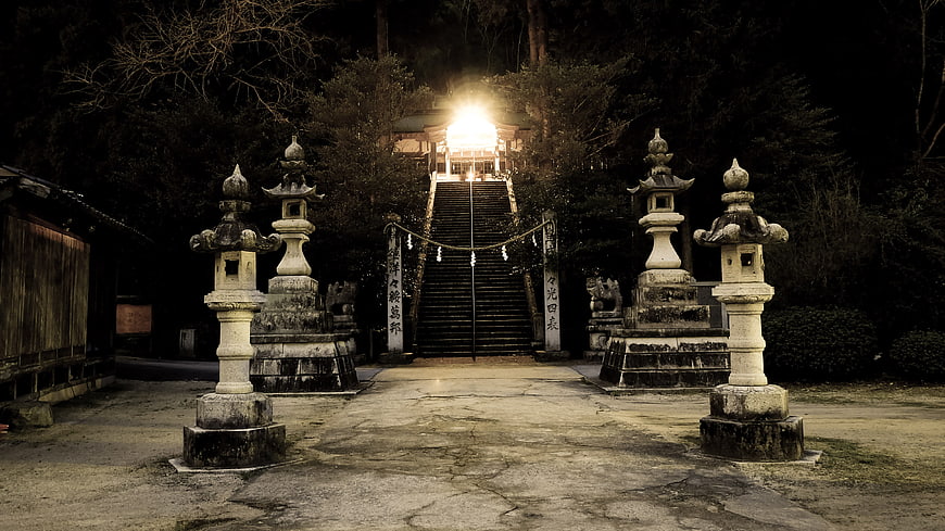 Japanese shrine entrance with stone lanterns and night lighting