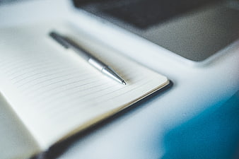 Close-up of silver pen on open notebook with laptop