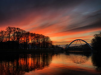 Dramatic Sunset Over River with Silhouetted Bridge and Trees