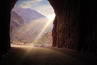 Sunlight Beams Through Desert Cave Tunnel to Mountain Landscape