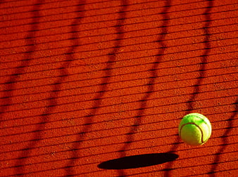 Tennis Ball on Red Clay Court with Net Shadows