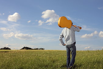 Man with Guitar in Green Meadow Under Blue Sky