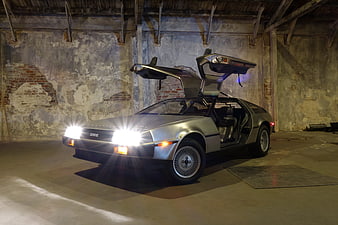 Silver DeLorean DMC-12 with gull-wing doors open in industrial warehouse
