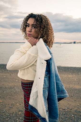 Stylish Woman with Curly Hair on Beach at Sunset