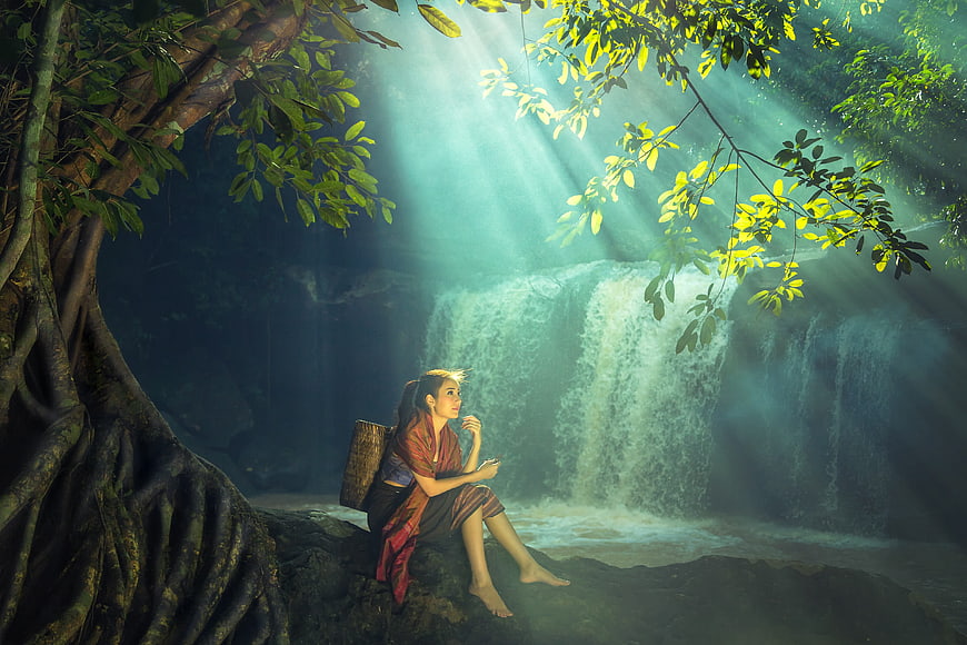 Asian Woman In Traditional Wear Sitting By Waterfall In Jungle