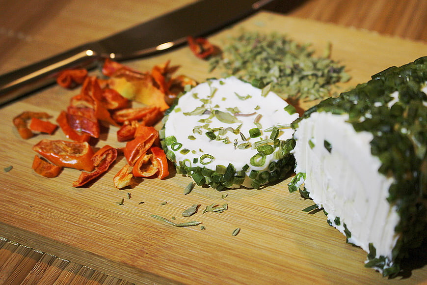Herb-crusted goat cheese log with sun-dried tomatoes on wooden board