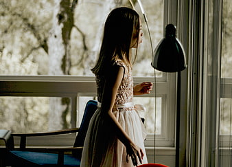 Young girl in pink dress standing by window