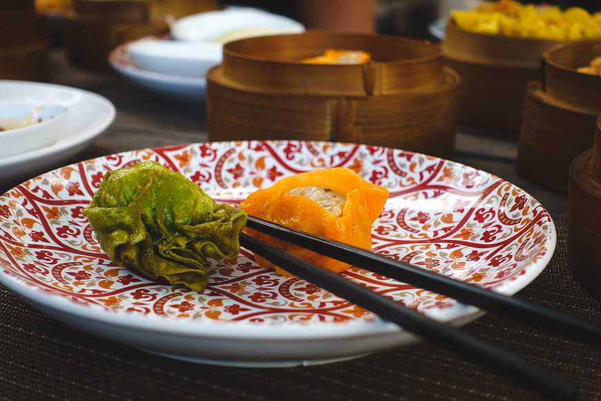 Colorful dim sum dumplings on patterned plate with chopsticks