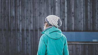 Woman in teal jacket and knit hat looking away
