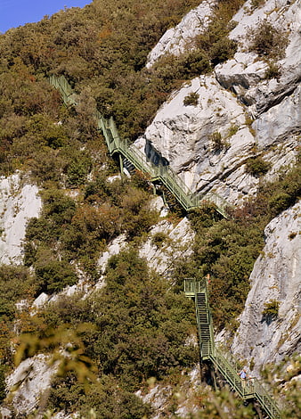 Green metal staircase winding up steep rocky mountain cliff