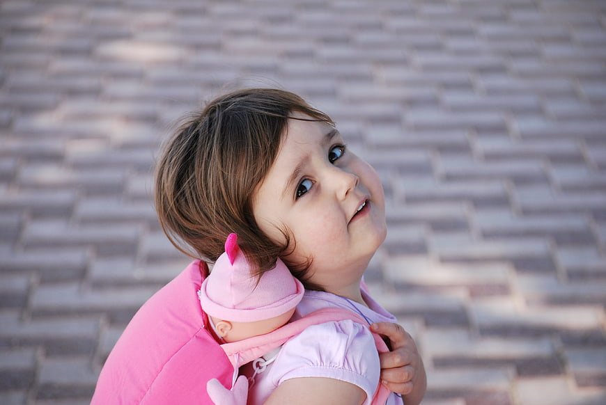 Cute little girl carrying pink doll backpack outdoors