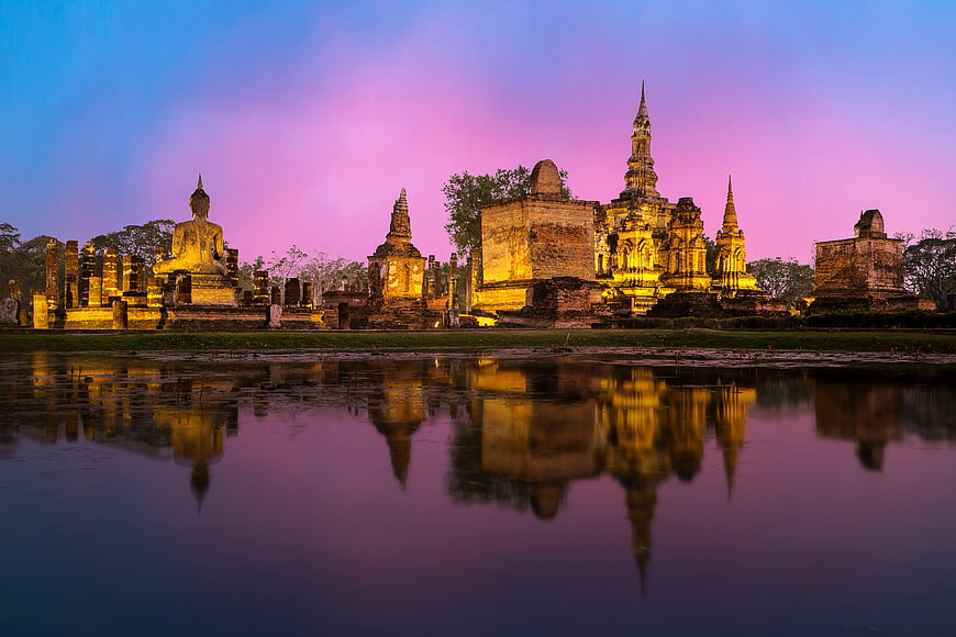 Illuminated Ancient Thai Temple Ruins Reflected in Water at Dusk