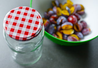 Glass jar with checkered lid and bowl of fresh plums