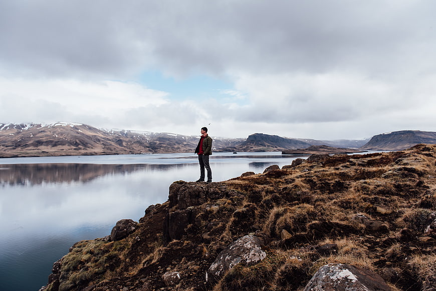 Man standing on rocky cliff overlooking lake and mountains