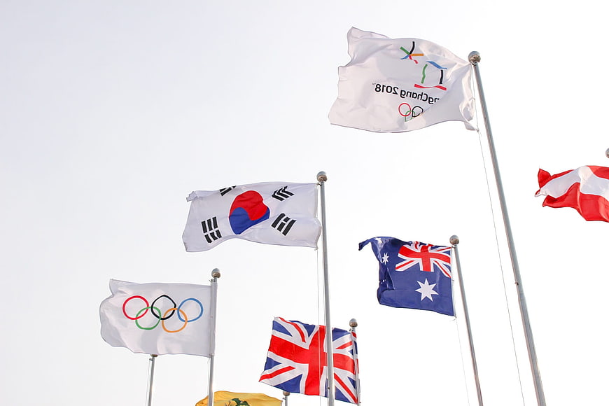 International Olympic and National Flags Flying Against White Sky