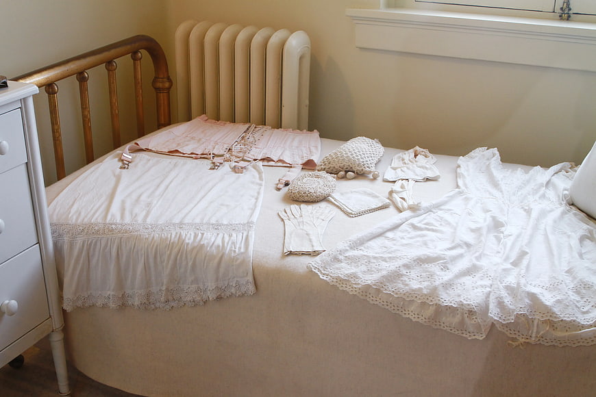 Vintage white lace baby clothes and pink outfit on bed