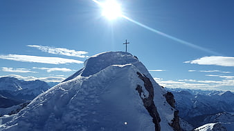 Summit Cross on Snowy Alpine Peak Under Bright Sun