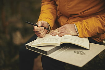 Man Writing in Journal Outdoors in Orange Jacket