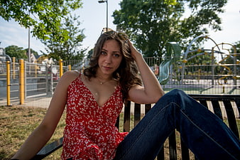 Young woman in red floral top sitting on park bench