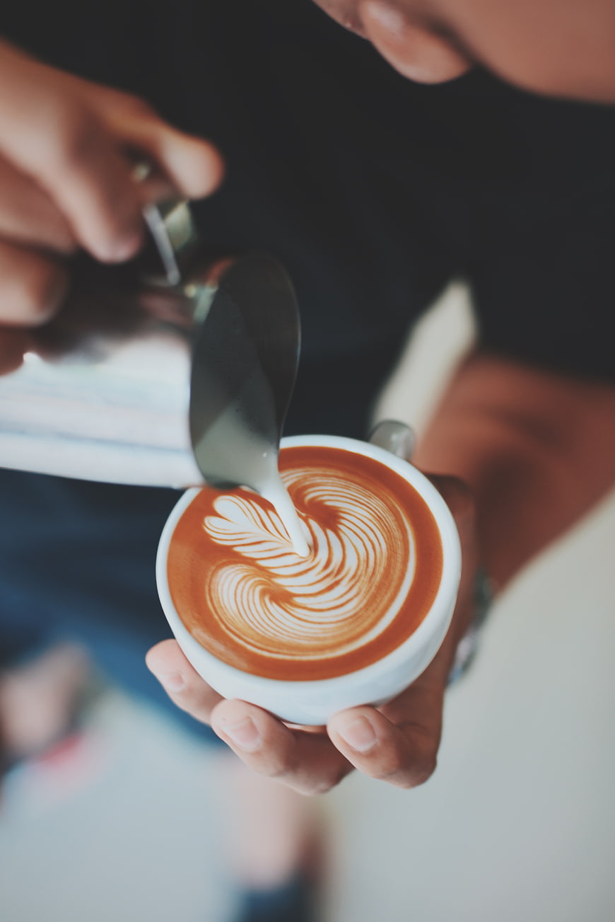 Barista pouring latte art in a white coffee cup