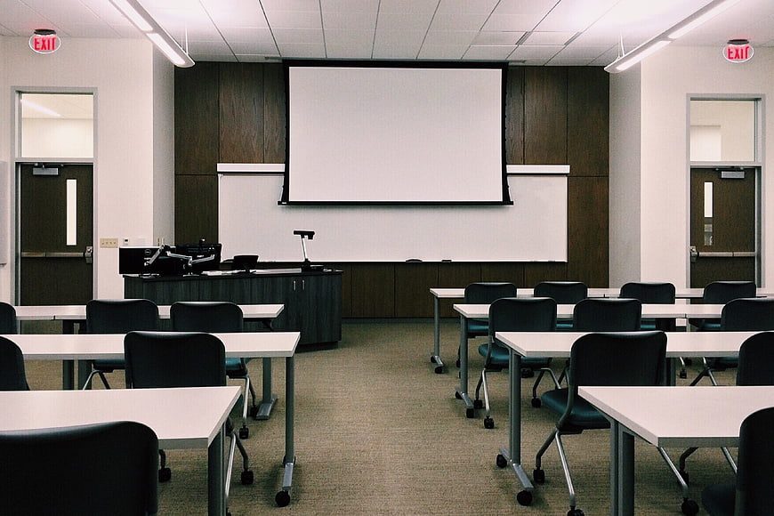Empty modern university classroom with rows of desks and projection screen