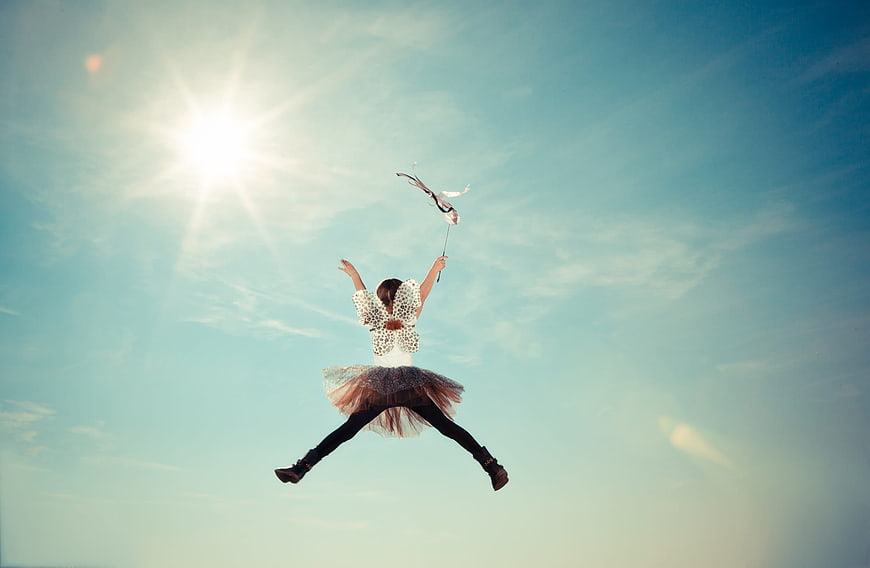 Girl in fairy costume jumping with wand against blue sky