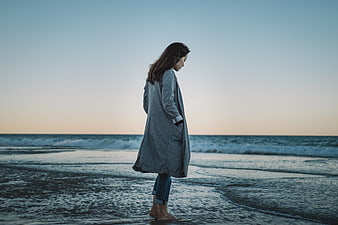 Woman standing barefoot on beach at dusk
