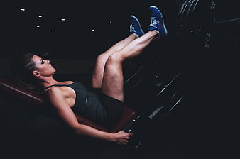 Woman performing leg press exercise in dark gym