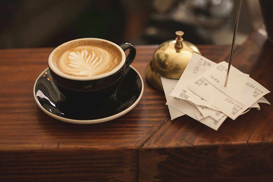 Latte Art Coffee Cup on Wooden Counter with Receipts