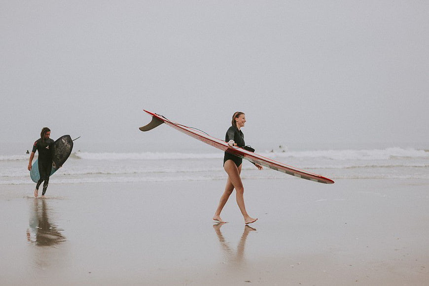 Woman Carrying Surfboard on Overcast Beach