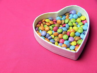 Heart-shaped box of colorful candies on pink background
