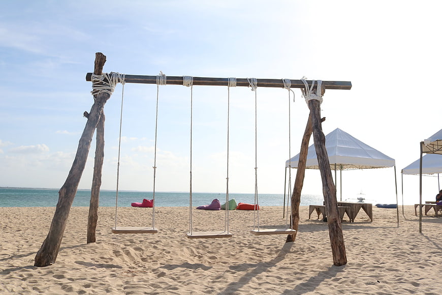 Rustic wooden swing set on sandy beach with ocean view