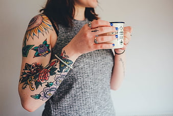 Woman with colorful arm tattoos holding a coffee mug