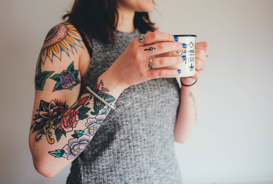 Woman with colorful arm tattoos holding a coffee mug