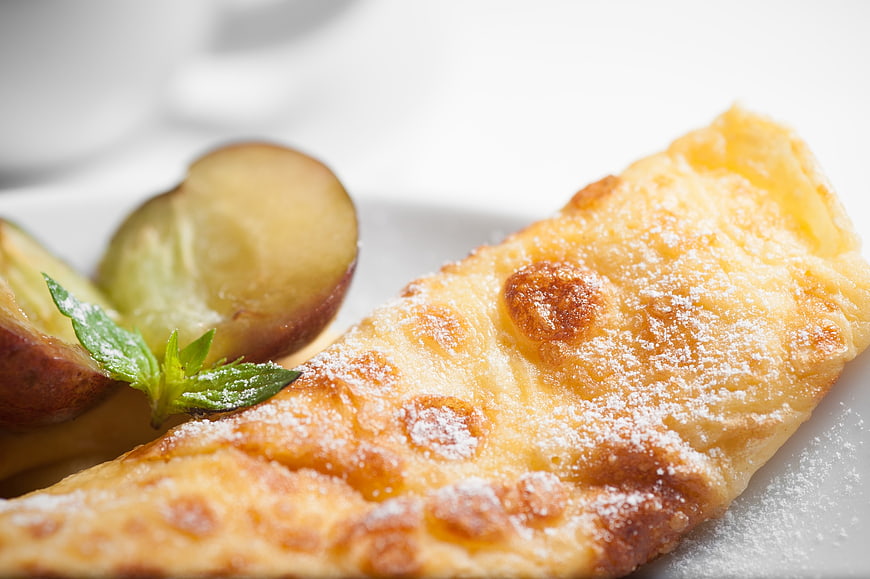 Close-up of golden apple strudel with powdered sugar and fresh fruit